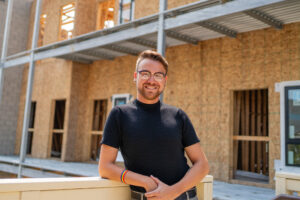 Evan stands in front of a building under construction - the future home of a 2SLGBTQ+ housing complex for older adults.