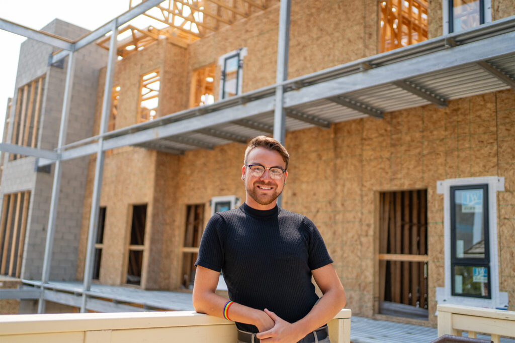 Evan stands in front of a building under construction - the future home of a 2SLGBTQ+ housing complex for older adults.
