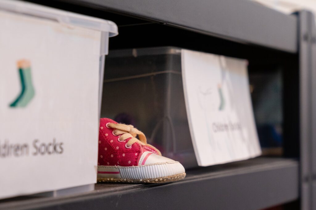 A pink polka dot child's shoe on a shelf peeks out between boxes of donated clothing.