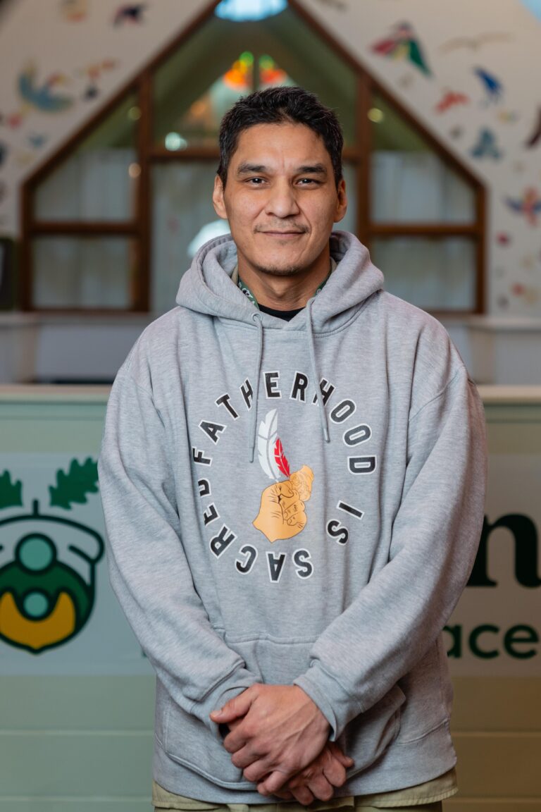 Phil stands proudly in the lobby at Acorn Family Place, wearing a grey hoodie that says "fatherhood is sacred."