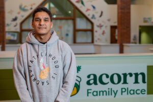 Phil stands proudly in the lobby at Acorn Family Place, wearing a grey hoodie that says "fatherhood is sacred."