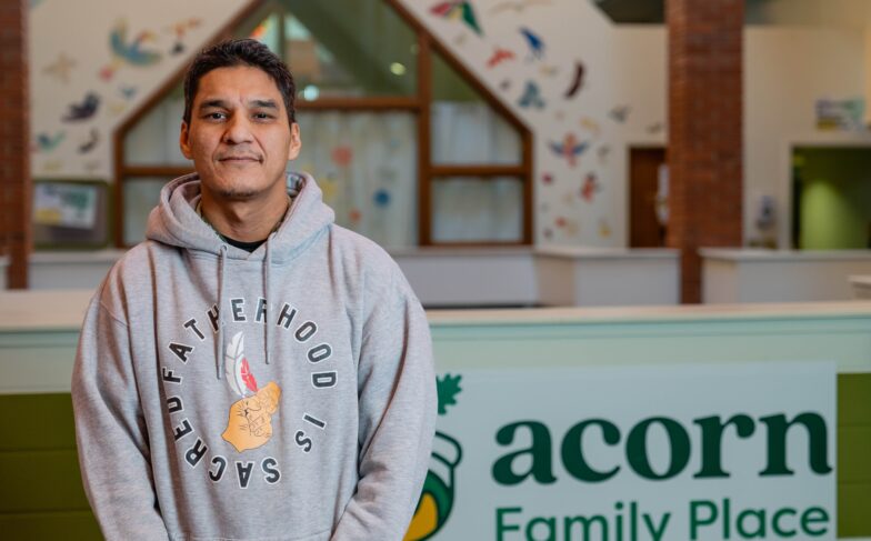 Phil stands proudly in the lobby at Acorn Family Place, wearing a grey hoodie that says "fatherhood is sacred."