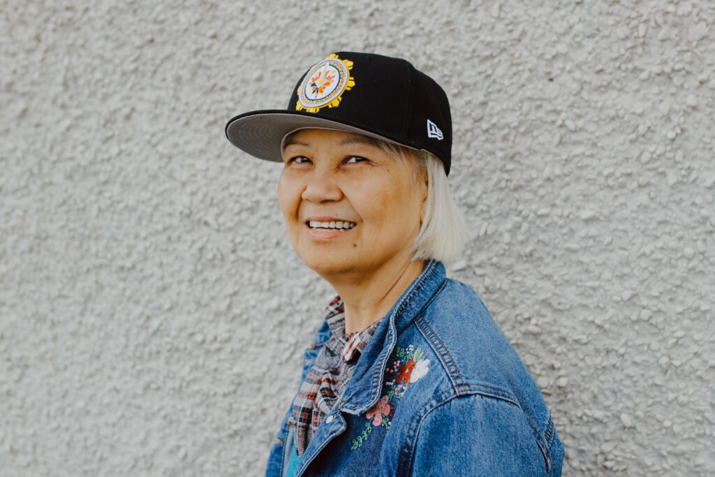 A guest wearing a black hat and jean jacket smiles proudly for their portrait after getting their hair styled.
