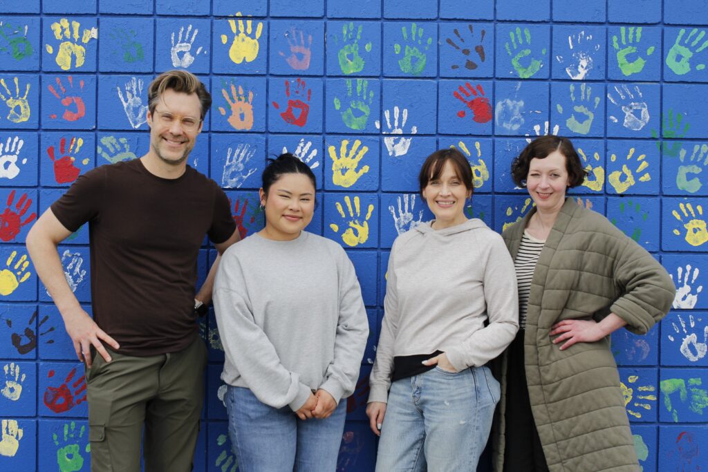 Four Mondetta team works stand against a blue wall with colourful painted handprints.
