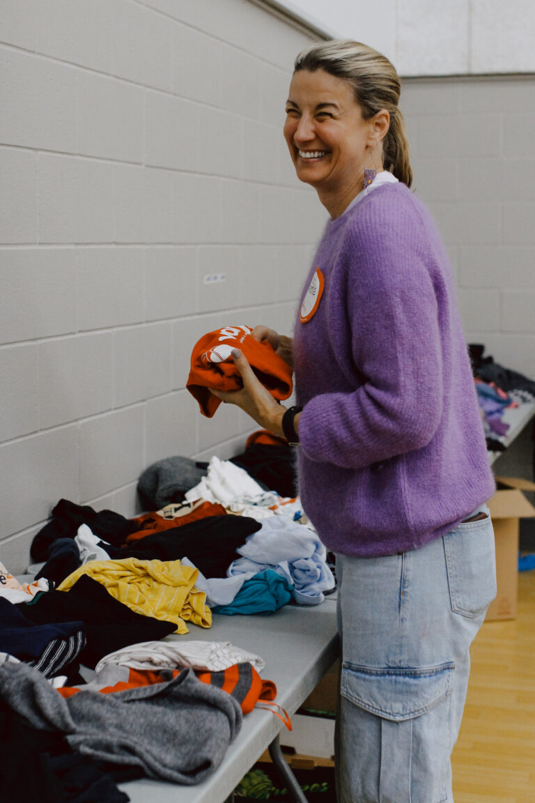 Kristie Pearson wears a purple sweater, jeans, and a bright smile as she folds a red shirt.